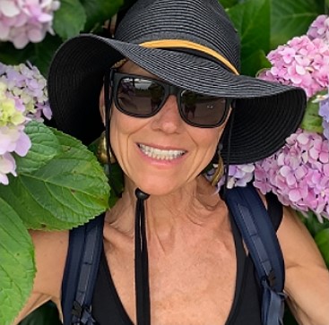 Karen, a woman receiving TRODELVY, is smiling at the camera. Karen is a White woman wearing a black sun hat and sunglasses.